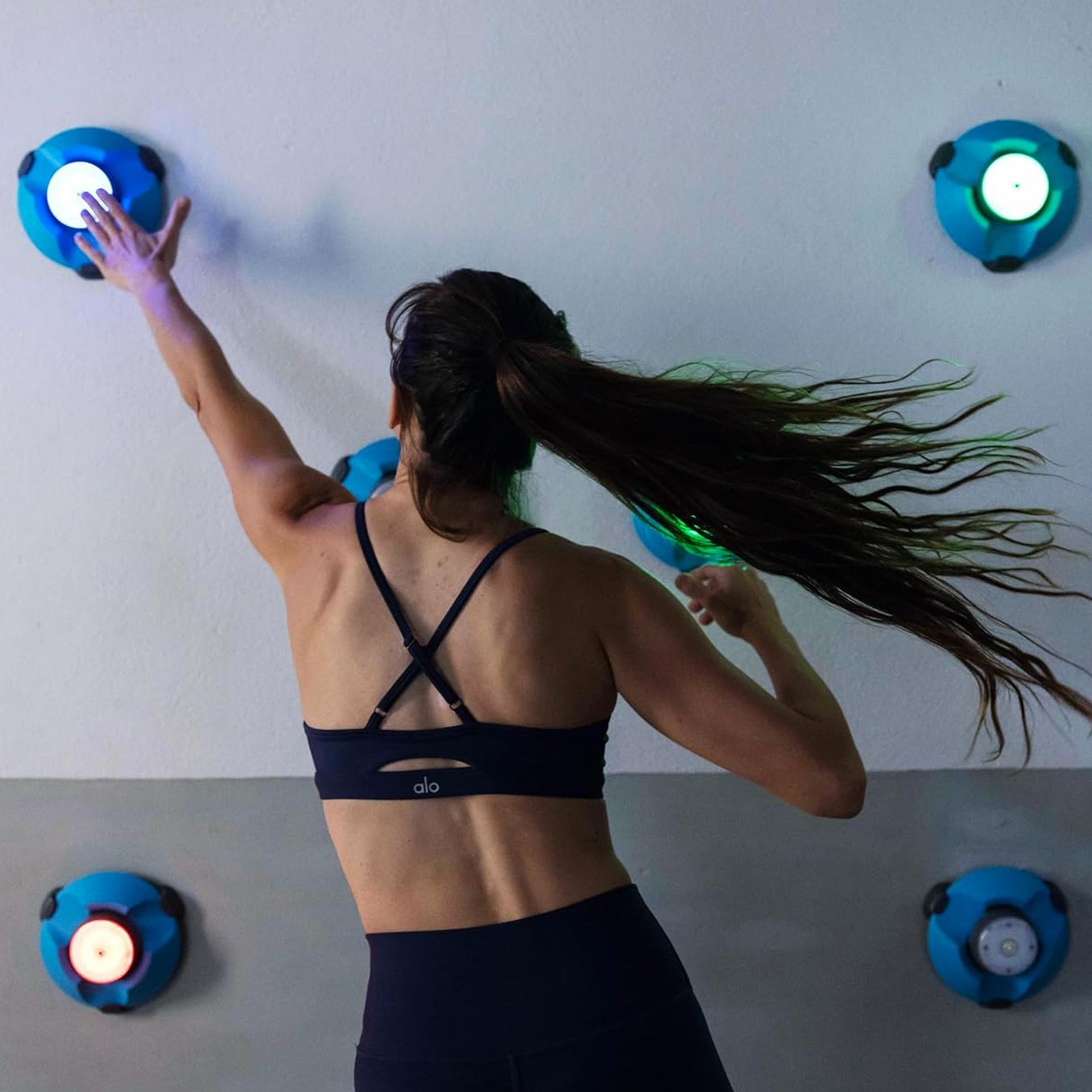 Woman exercising with colorful lights on a wall, reaching upwards in athletic attire.