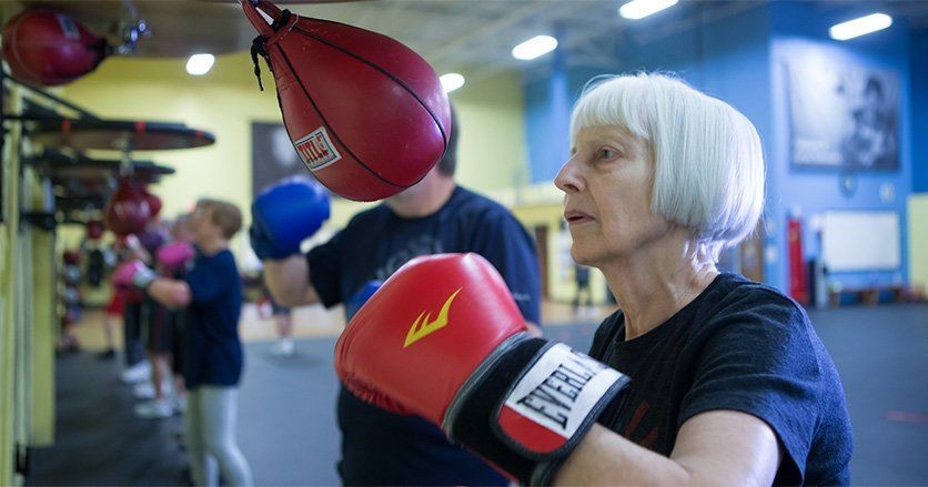 Participants wearing boxing gloves practicing with a speed bag in a gym.
